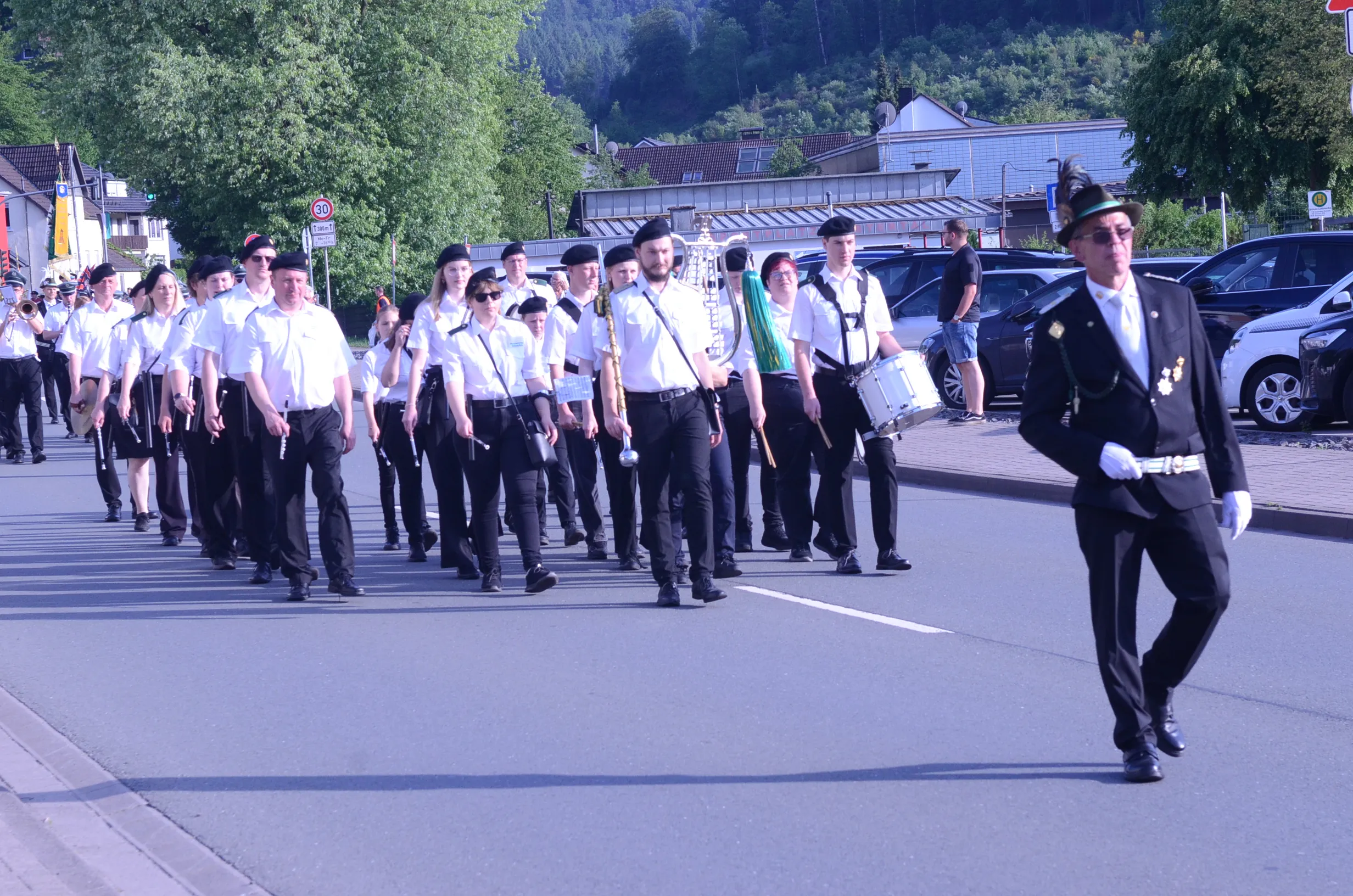 Eine Gruppe von Musiker:innen und Mitgliedern einer Schützenkompanie marschiert auf einer Straße, angeführt von einer Person in historischer Uniform.