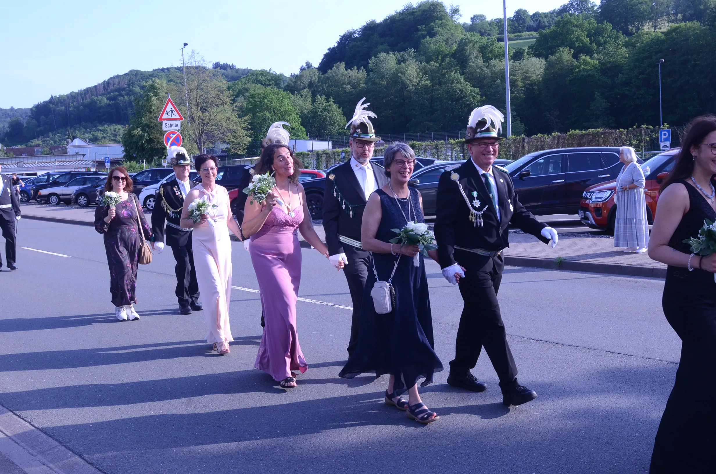 Festzug mit mehreren Personen in festlicher Kleidung, darunter Mitglieder einer Schützenkompanie mit Uniformen und Hüten, sowie Damen in Abendkleidern, die Blumensträuße tragen.