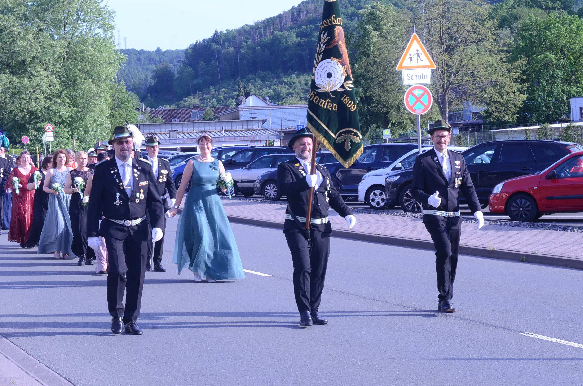 Festzug in Oestertal mit vier Personen in historischen Uniformen, die eine grüne Fahne mit Wappen tragen. Im Hintergrund sind Zuschauer und geparkte Autos zu sehen.