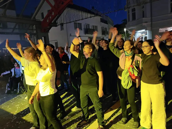 Menschen tanzen mit erhobenen Händen bei Nacht unter bunten Lichtern auf dem Plettenberger Stadtfest.