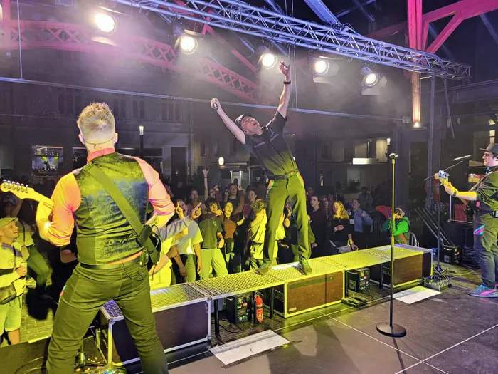 Ein Sänger der Band Hitfluencer performt mit erhobenen Armen auf einer beleuchteten Bühne vor einem Publikum beim Plettenberger Stadtfest.