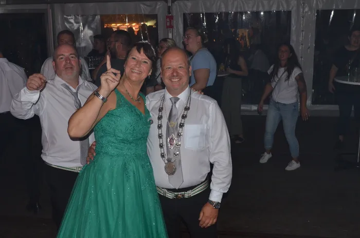 Ein Mann mit einer zeremoniellen Amtskette und eine Frau in einem grünen Glitzerkleid lächeln in einem Festzelt.