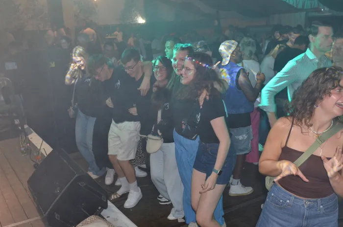 Eine Gruppe junger Menschen tanzt und feiert in einem Festzelt unter farbiger Partybeleuchtung.