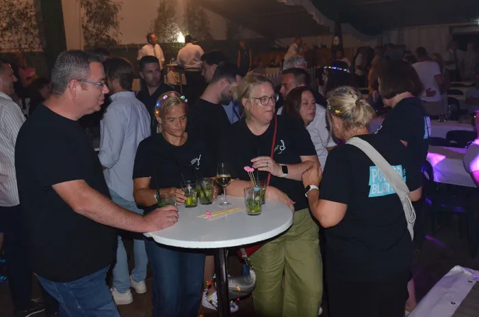 Eine Gruppe von Menschen steht um einen kleinen weißen Stehtisch mit Getränken in einem Festzelt.