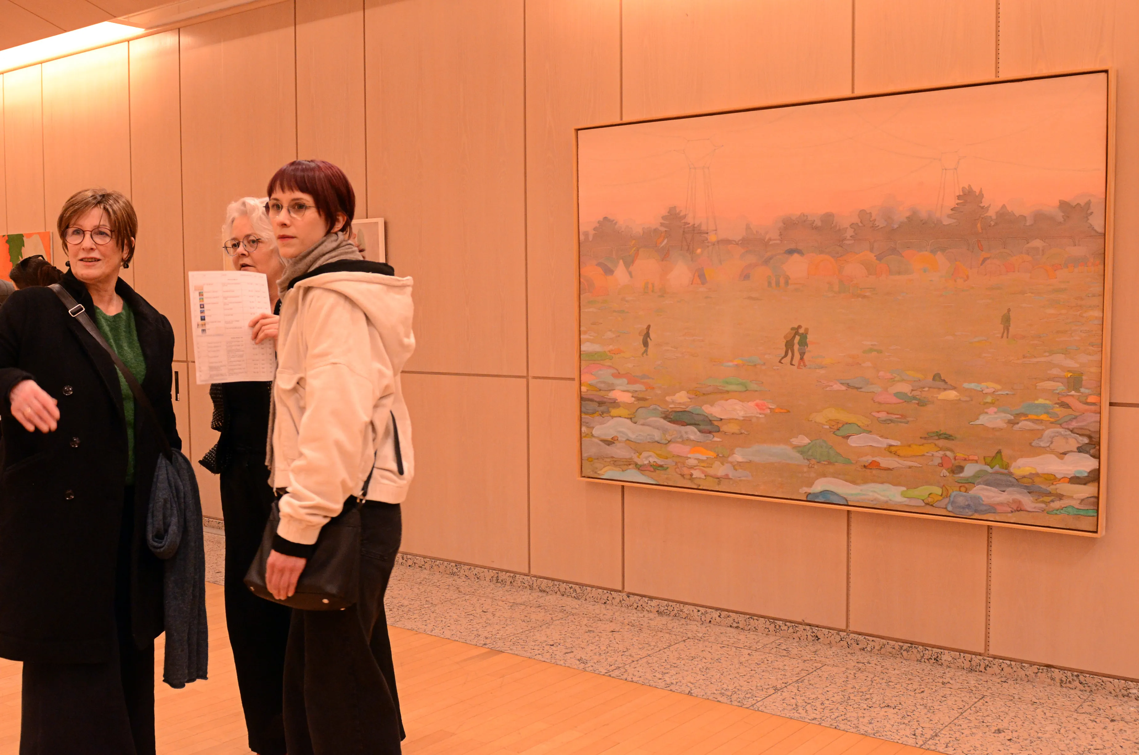 Drei Frauen betrachten ein großes Gemälde in einem hellen Raum, vermutlich während der Ausstellung für das Werkstatt-Stipendium.