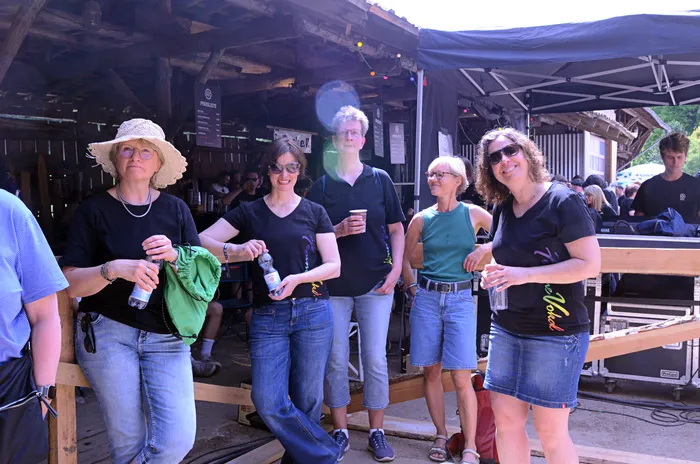 Vier Frauen stehen lächelnd vor einer Bühne auf dem Immecke Rock Festival, jede hält Getränke in der Hand.