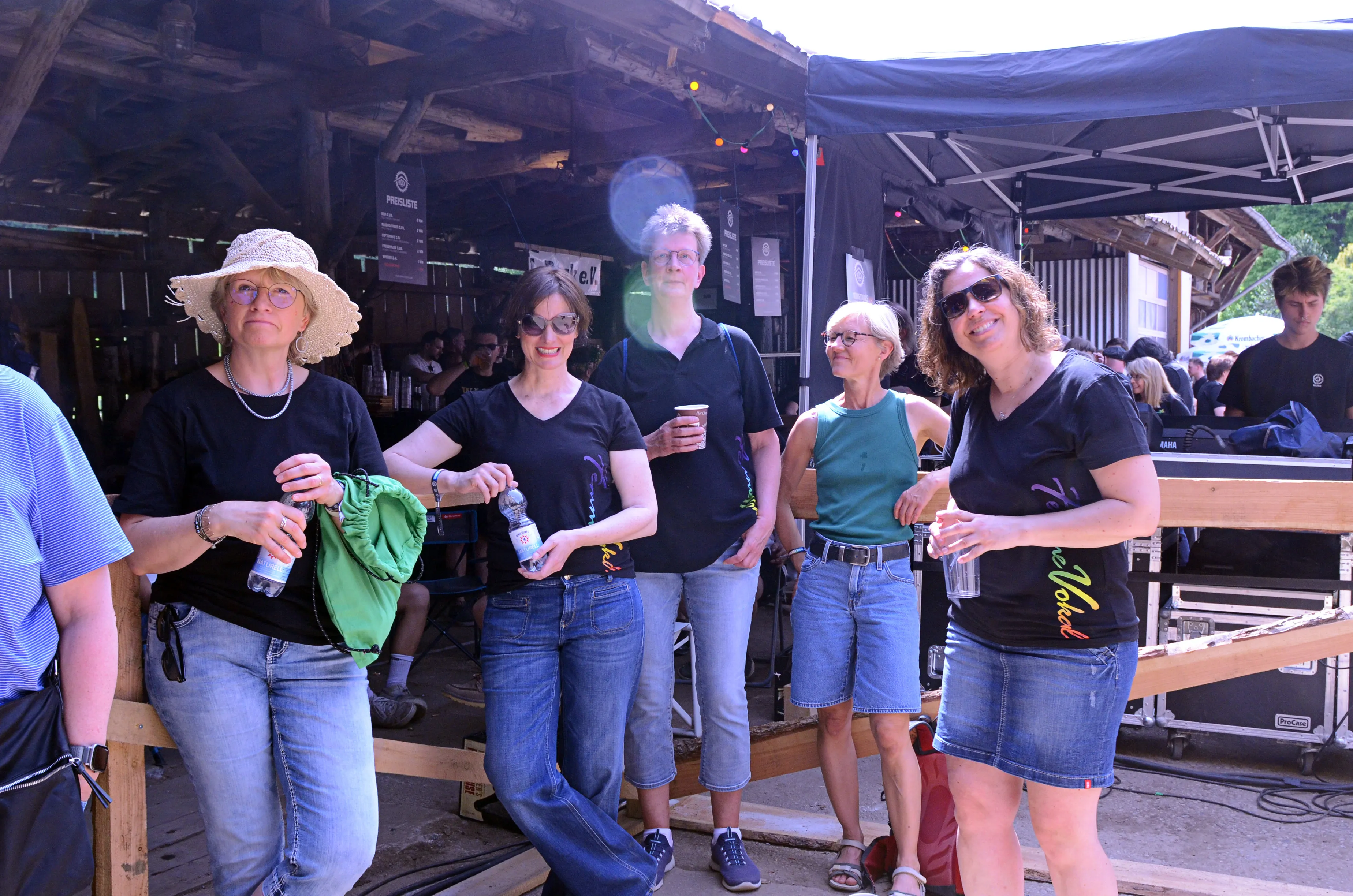 Vier Frauen stehen lächelnd vor einer Bühne auf dem Immecke Rock Festival, jede hält Getränke in der Hand.
