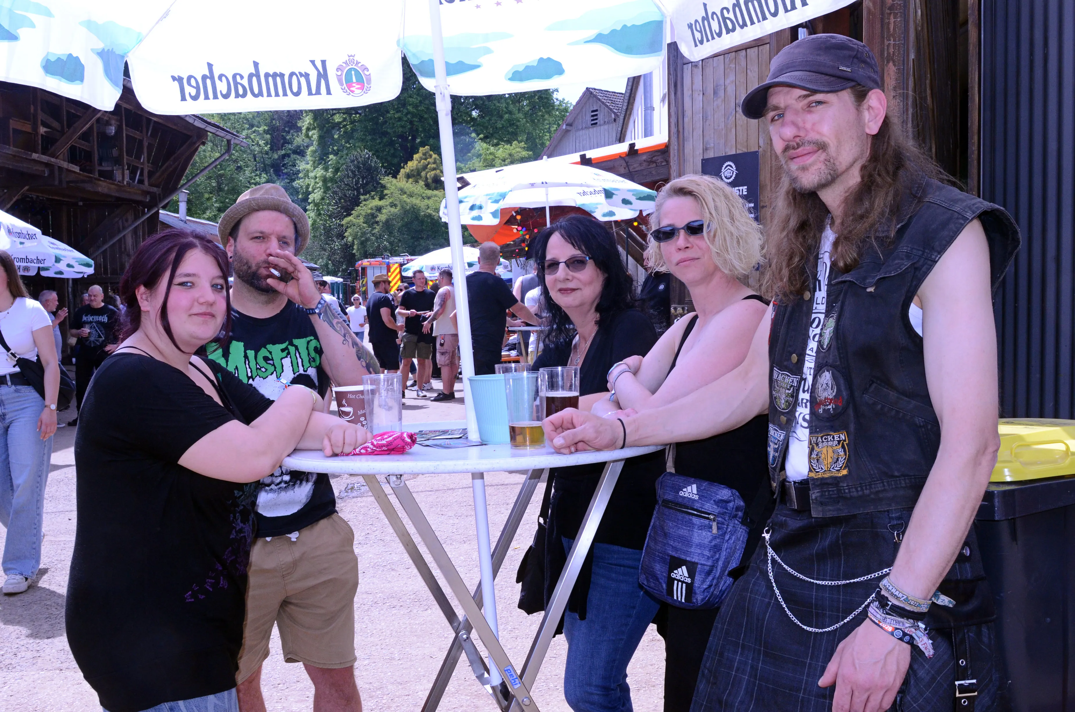 Fünf Personen stehen um einen kleinen Tisch auf dem Gelände des Immecke Rock Festivals. Sie halten Biergläser und unterhalten sich.