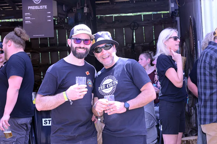Zwei Männer mit Sonnenbrillen und ein Bier in der Hand stehen vor einer Menschenmenge auf dem Immecke Rock Festival.