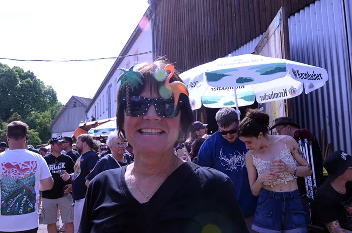 Nahaufnahme einer Frau mit auffälligem Kopfschmuck und Sonnenbrille inmitten einer Menschenmenge auf dem Immecke Rock Festival.