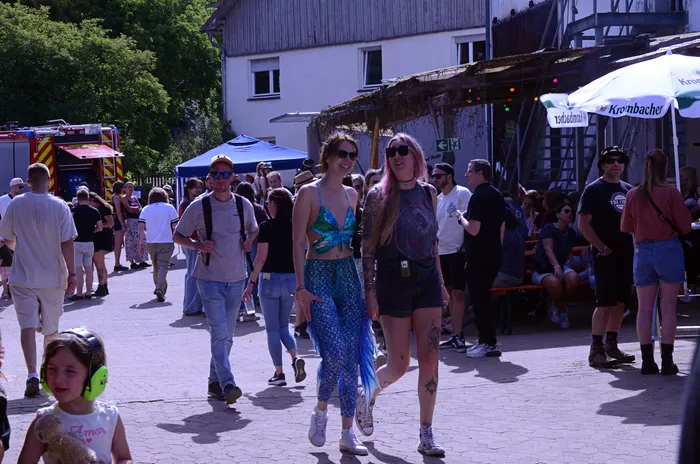 Menschenmengen bewegen sich auf einem Festivalgelände mit Bühnen und Essensständen. Im Hintergrund ein rotes Feuerwehrfahrzeug.