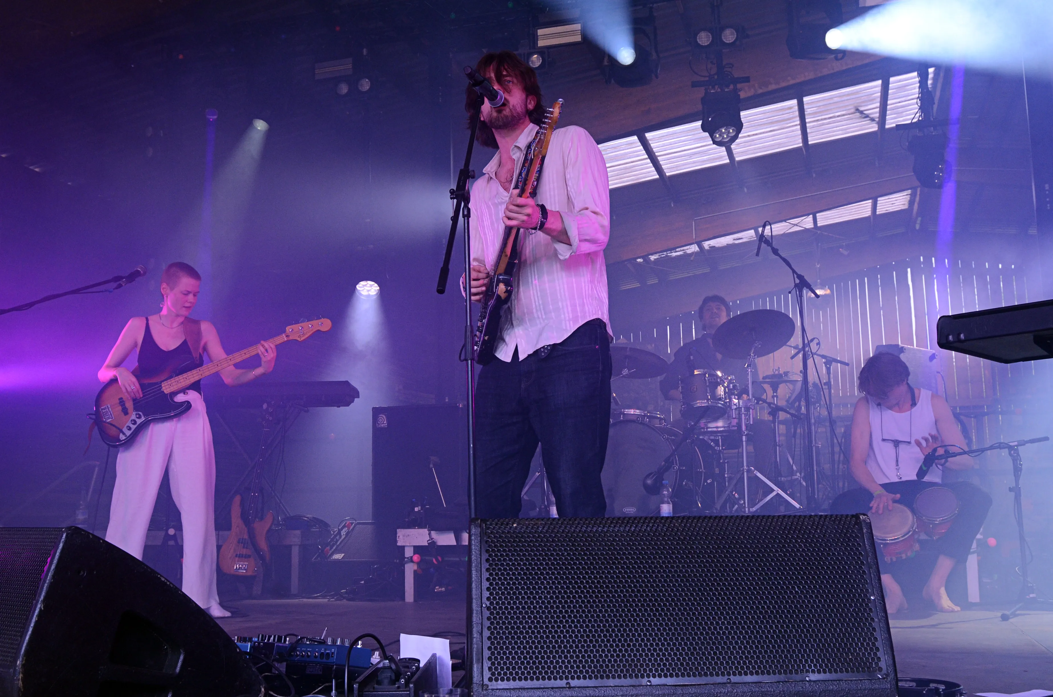 Band spielt auf einer Bühne vor Publikum bei dem Immecke Rock Festival in Plettenberg. Im Vordergrund steht der Gitarrist mit Mikrofon, links die Bassistin und rechts der Schlagzeuger.