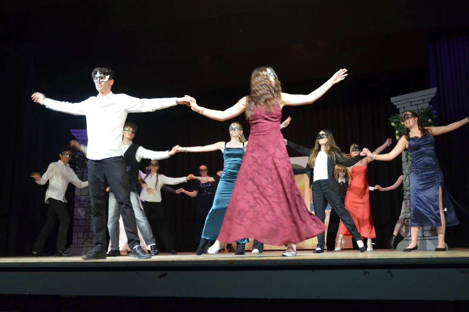 Szene aus der Theateraufführung „Viel Lärm um nichts“ mit Schülerinnen und Schülern in Kostümen und Masken, die im Kreis tanzen.