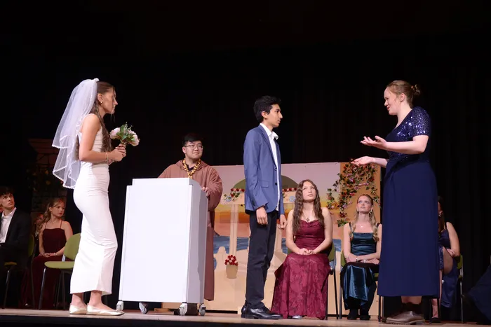 Szene aus Shakespeares „Viel Lärm um nichts“ mit einer Darstellerin im Brautkleid, einem Mann im Anzug und weiteren Ensemblemitgliedern auf einer Bühne.