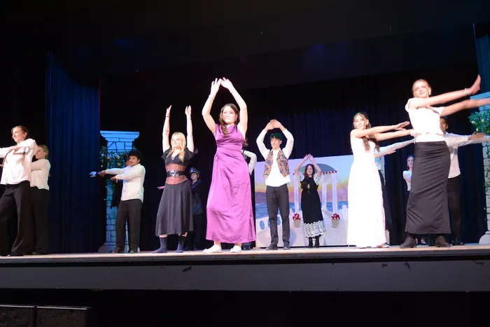 Ensemble des Albert-Schweitzer-Gymnasiums führt eine Szene aus Shakespeares „Viel Lärm um nichts“ auf, die Darsteller stehen in Kostümen auf einer Bühne vor einem dunklen Hintergrund und bewegen ihre Arme.
