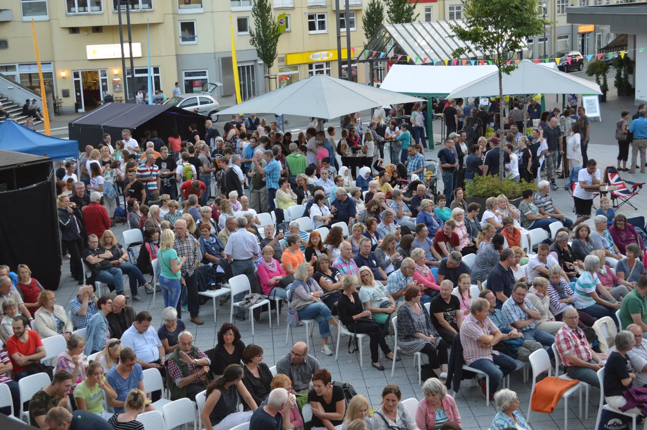 Viele Menschen sitzen auf weißen Stühlen auf dem Rathausplatz in Schalksmühle bei einem Open-Air-Kino unter weißen Zelten.