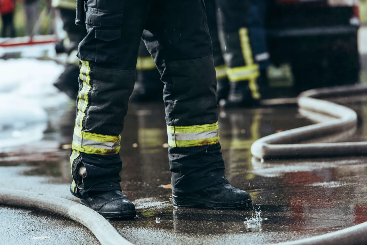 Feuerwehrstiefel und -hose stehen im Wasser, daneben ein Schlauch.