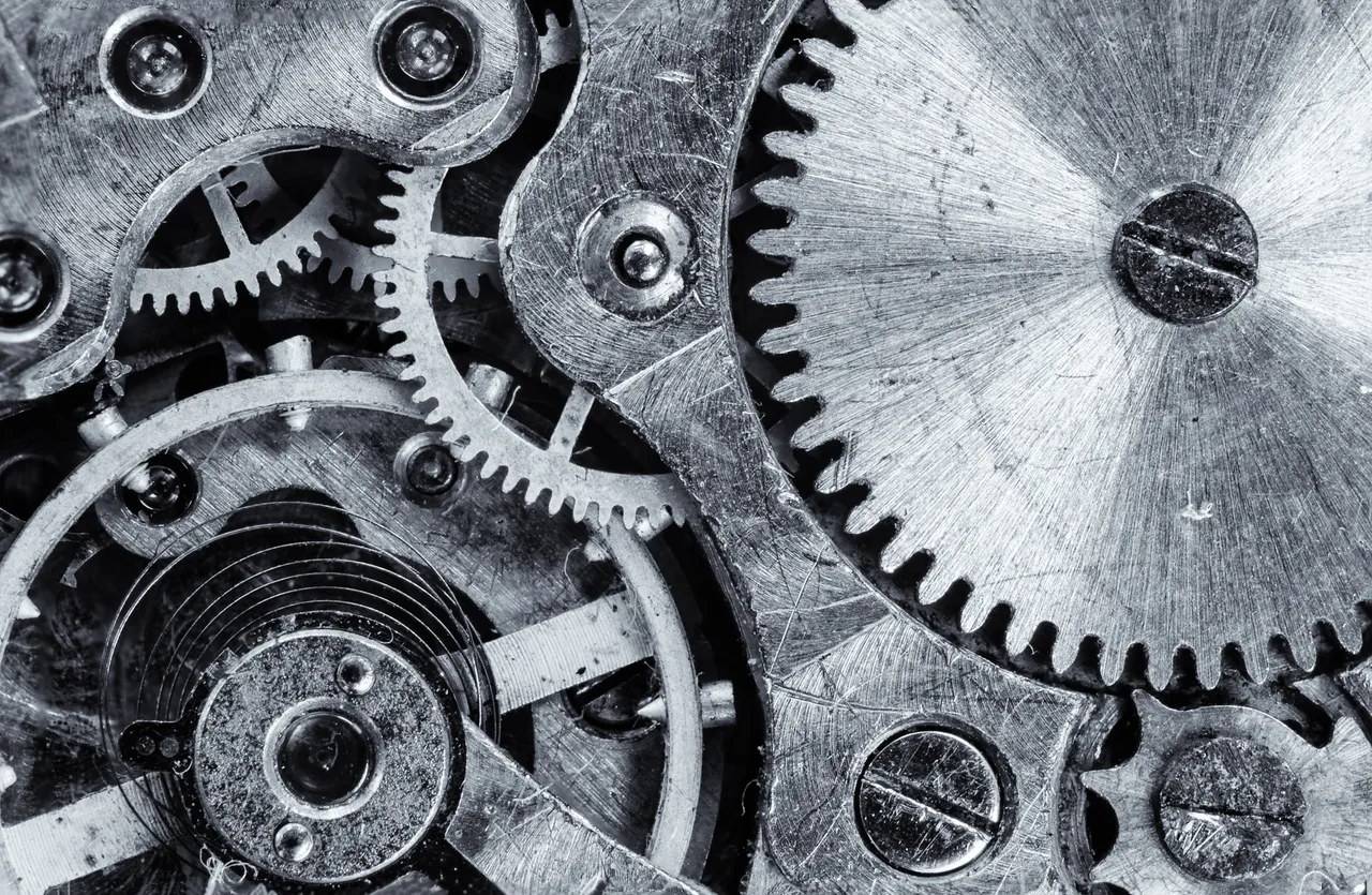 Nahaufnahme von Zahnrädern und mechanischen Teilen aus Metall, die ein komplexes Uhrwerk oder eine Maschine bilden.