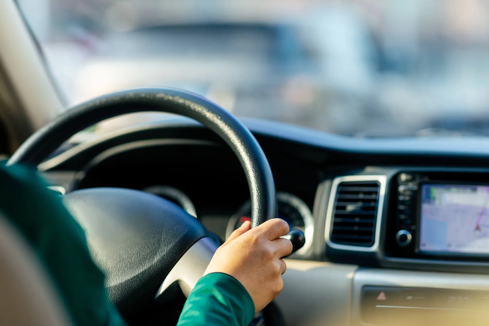 Eine Hand hält das Lenkrad eines Autos, während das Armaturenbrett mit einem Navigationssystem sichtbar ist.