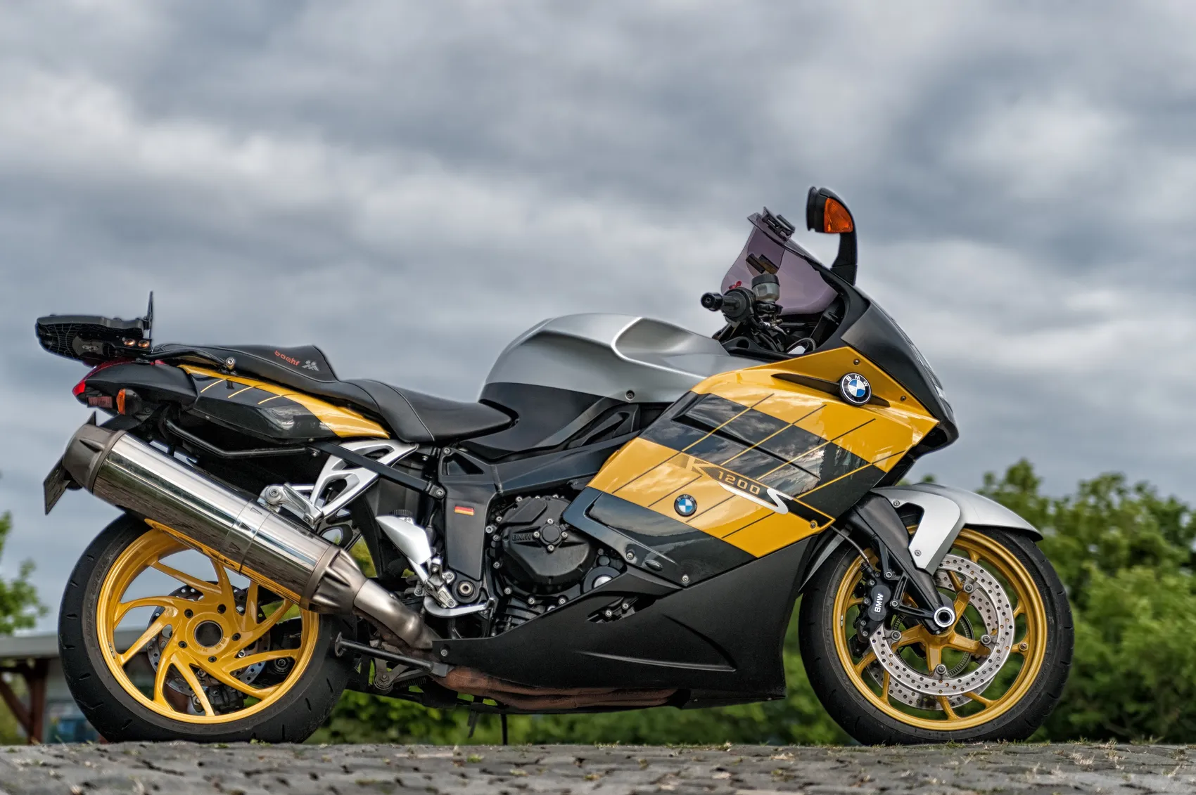 Ein schwarz-gelbes BMW-Motorrad mit silbernem Tank und gelben Felgen vor einem bewölkten Himmel.