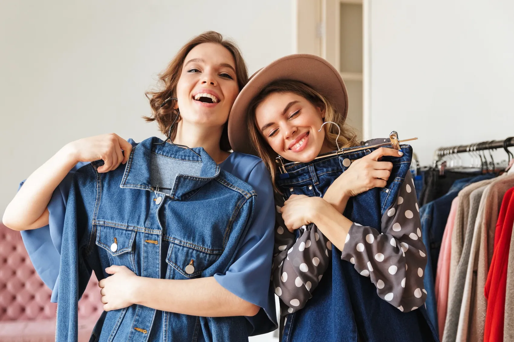 Zwei junge Frauen lachen und halten sich gegenseitig Kleidung vor, während sie in einem Geschäft oder Kleiderschrank stehen.