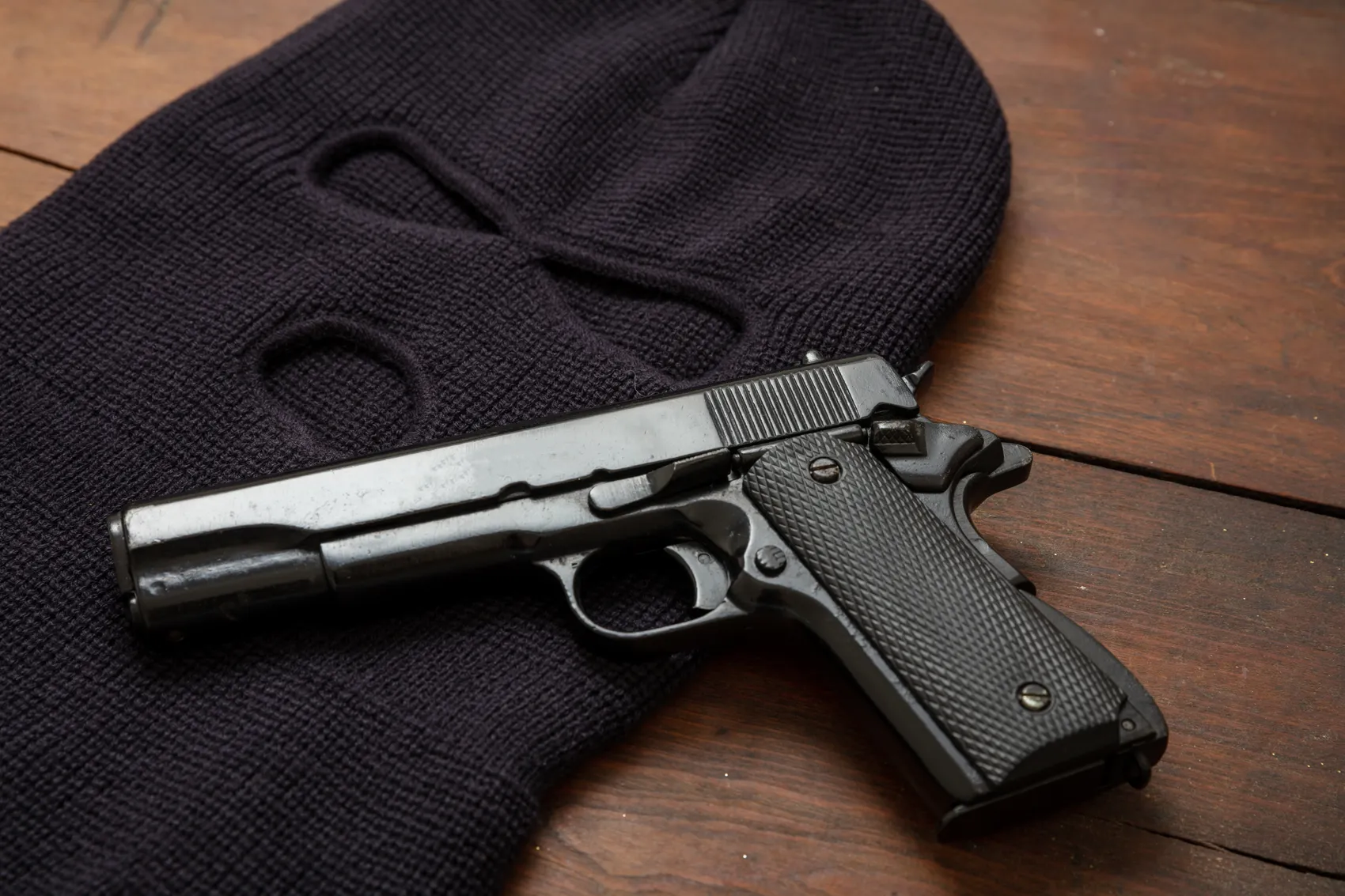 Eine schwarze Pistole liegt auf einem dunklen Strickpullover auf einem Holztisch. Das Bild dient als Symbol für einen Raubüberfall.