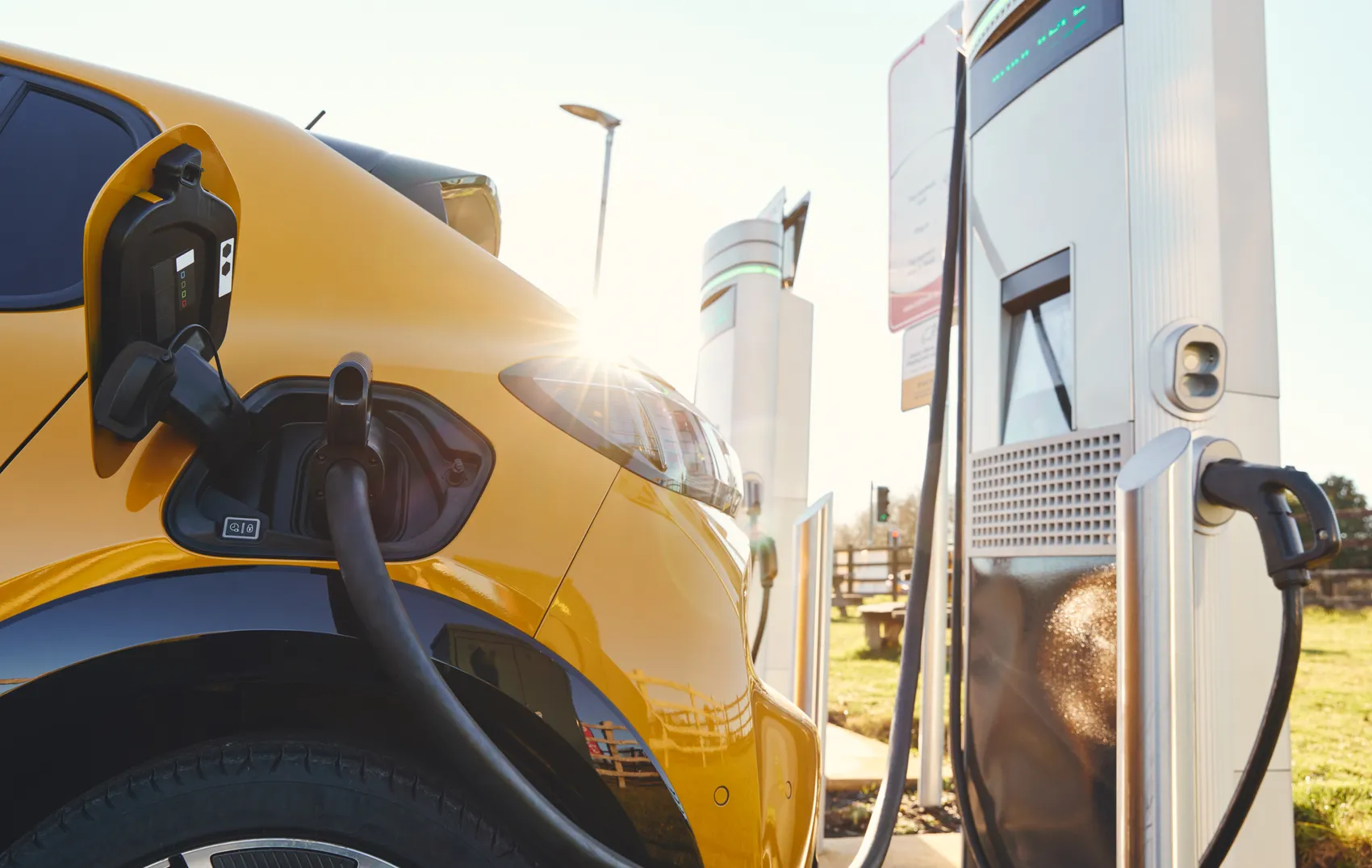 Gelbes Elektroauto wird an einer Ladestation aufgeladen, die Sonne scheint.