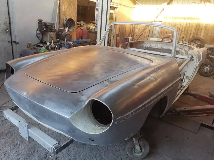 Die unlackierte Karosserie eines Oldtimers auf einem Metallgestell in einer Werkstatt.