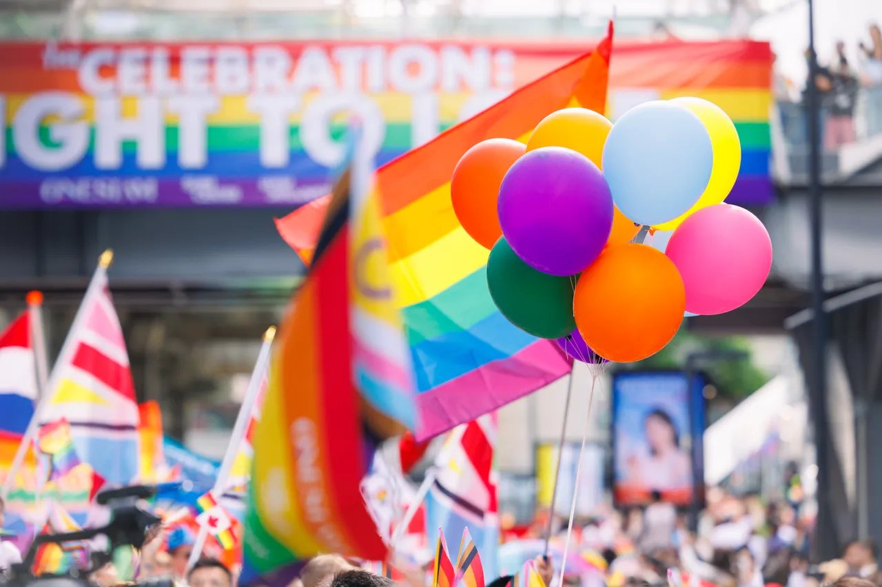 Bunte Luftballons vor Regenbogenfahnen und einem Banner mit der Aufschrift „Celebration“ bei einer Pride-Parade.