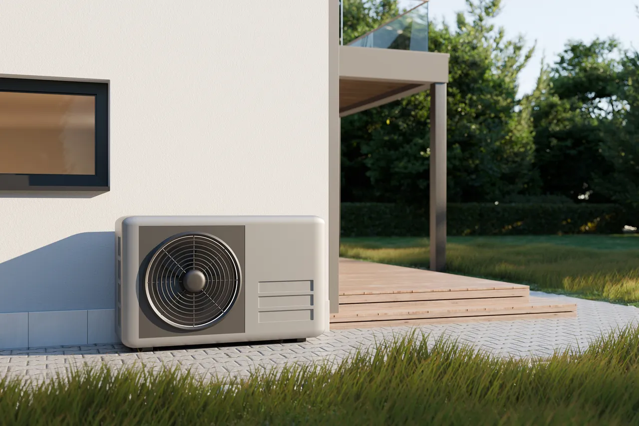 Wärmepumpe an der Außenwand eines modernen Hauses mit Garten im Hintergrund.