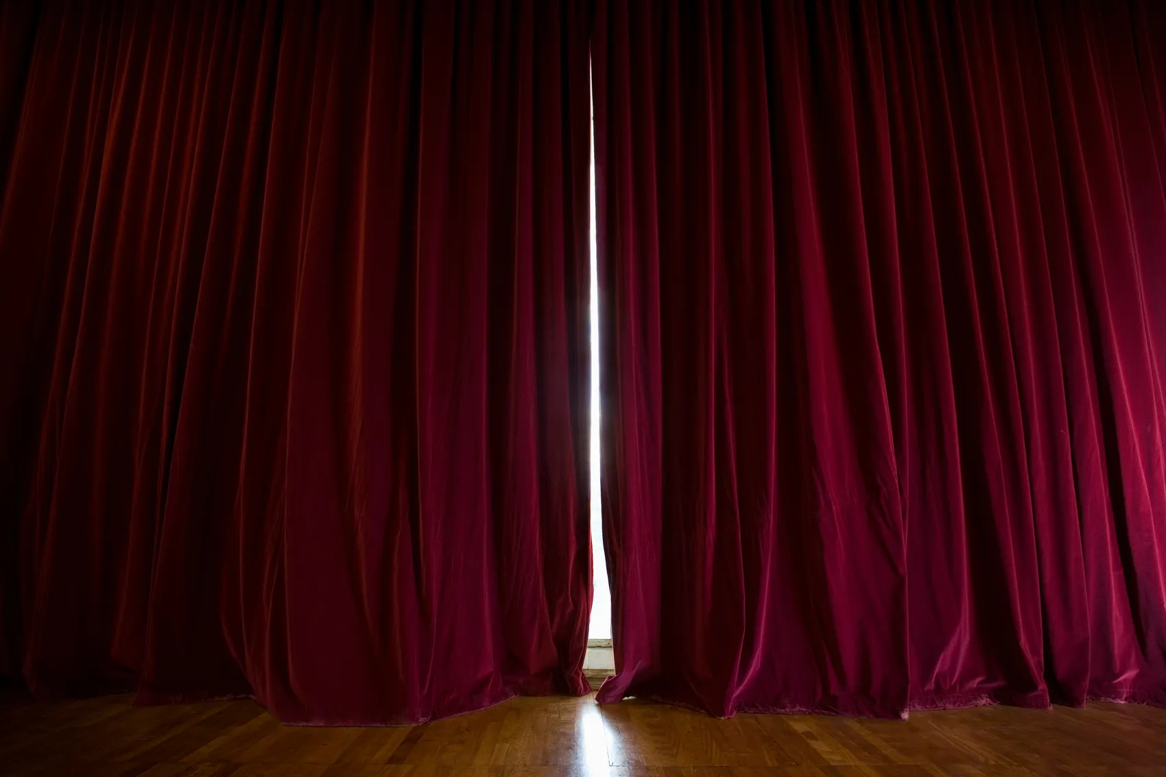 Ein geöffneter Vorhang aus rotem Samt gibt den Blick auf eine helle Bühne frei.