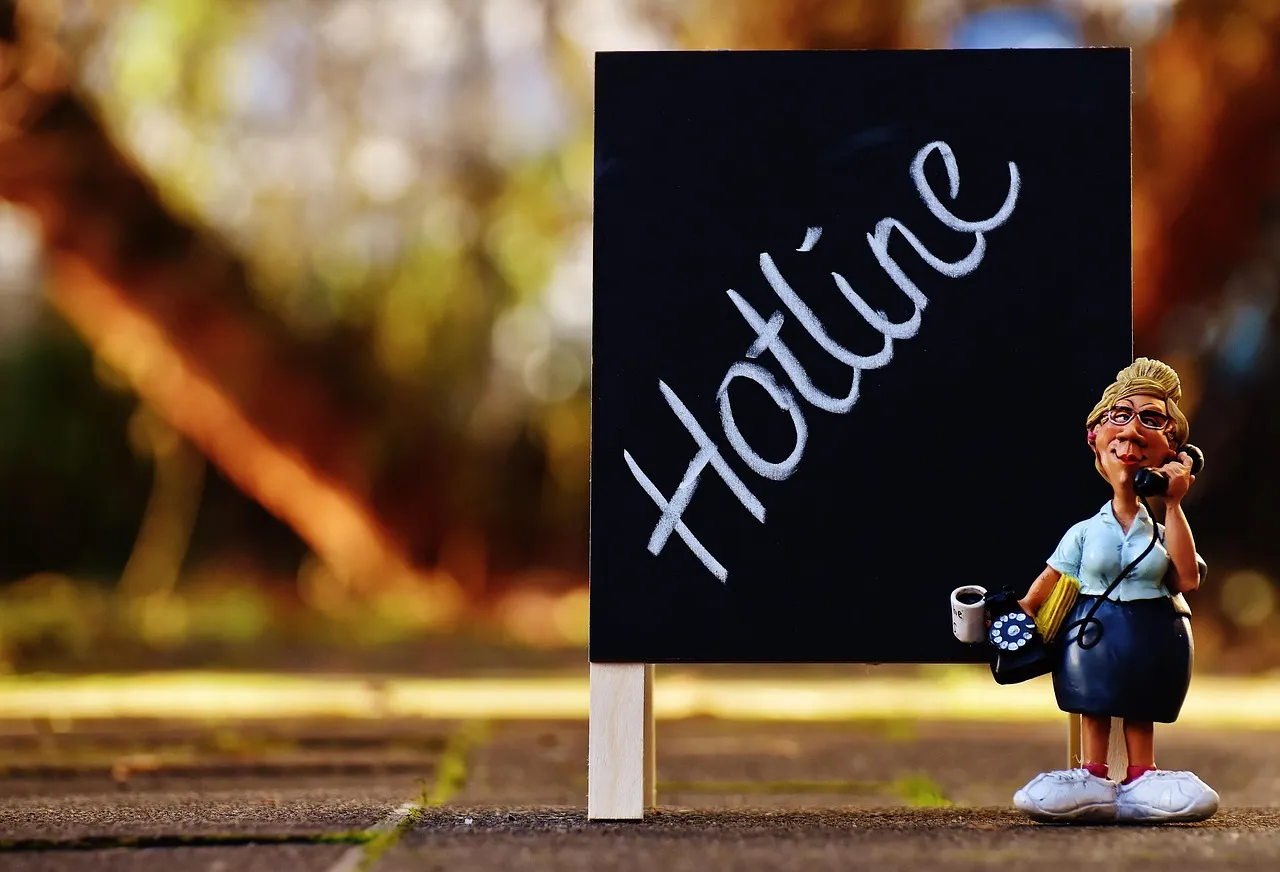 Figurine einer Sekretärin mit Telefonhörer neben einem Schild mit der Aufschrift „Hotline“.