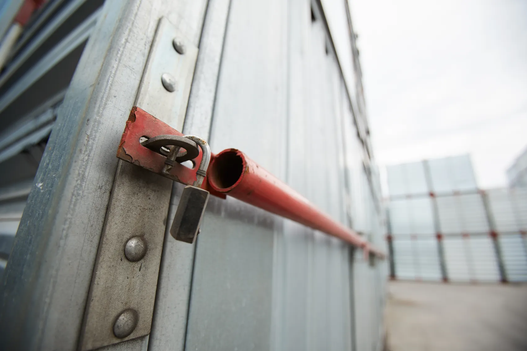 Ein Vorhängeschloss sichert eine rote Metallstange an einem grauen Metallcontainer.