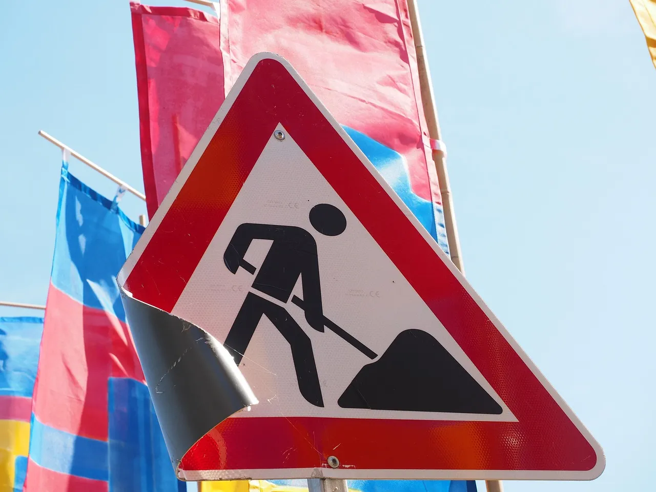 Dreieckiges Warnschild mit schwarzer Silhouette einer Person, die mit Schaufel arbeitet, vor rotem Hintergrund.