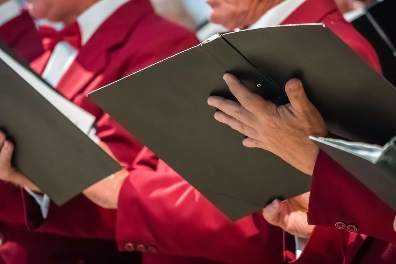 Chormitglieder in roten Jacken halten Notenblätter und singen gemeinsam.
