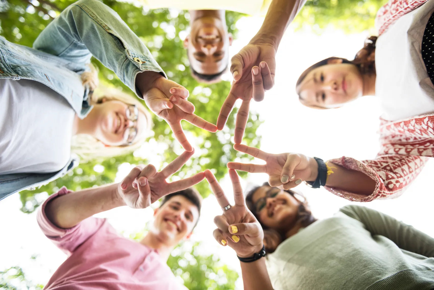Eine Gruppe junger Menschen formt mit ihren Händen im Freien ein Stern-Symbol. Die Aufnahme ist von unten fotografiert und zeigt die lächelnden Gesichter der Gruppe.