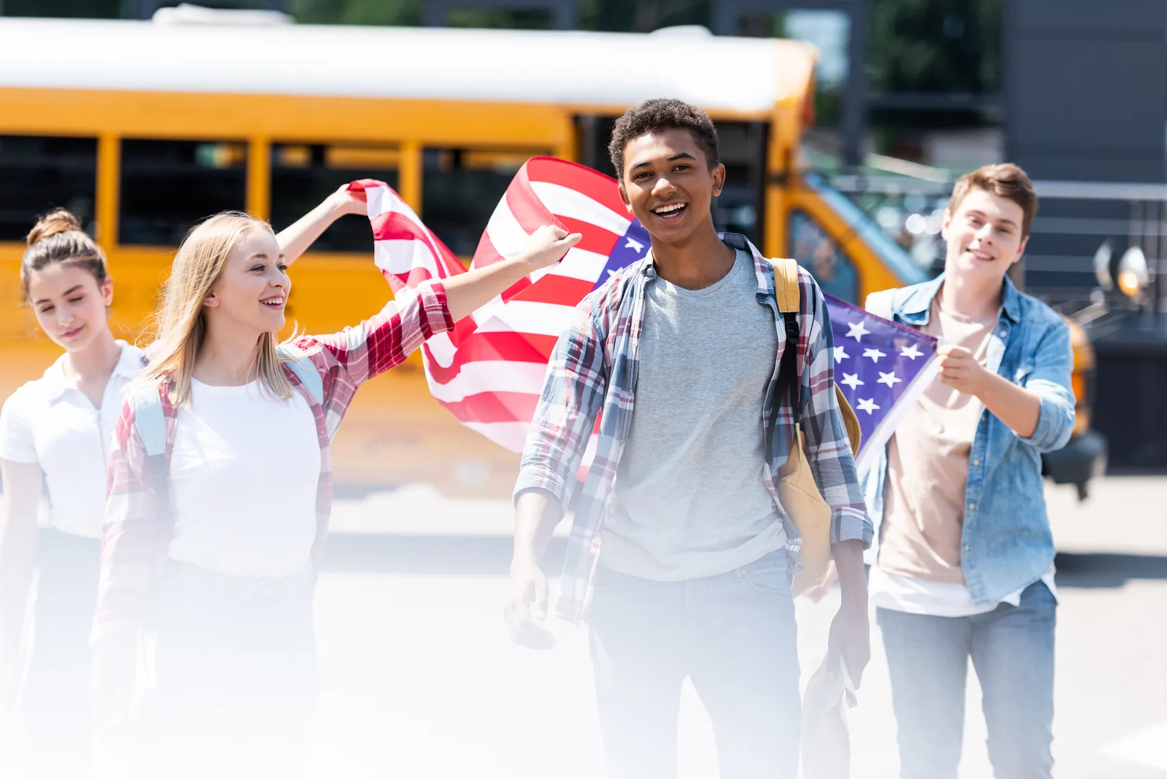 Schülergruppe mit US-amerikanischen Flaggen vor einem Schulbus, lächelnd in die Kamera blickend.
