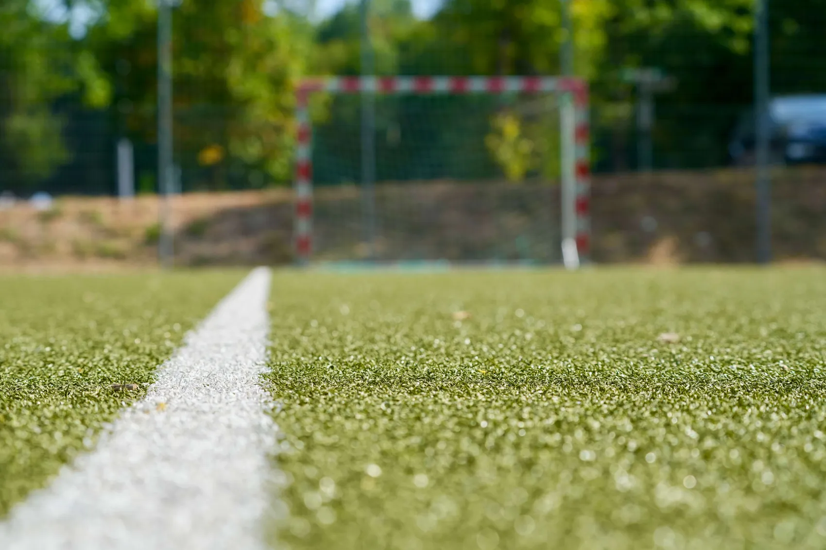 Weiße Markierungslinie auf grünem Kunstrasen mit einem unscharfen Fußballtor im Hintergrund.