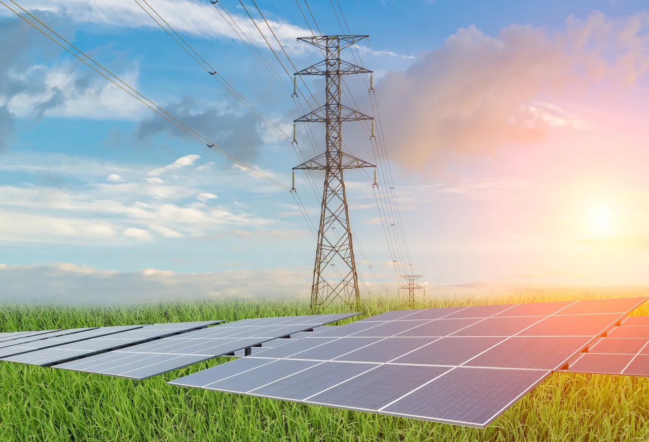 Solaranlage im Grünen vor blauen Himmel und Strommast, die für erneuerbare Energien steht.