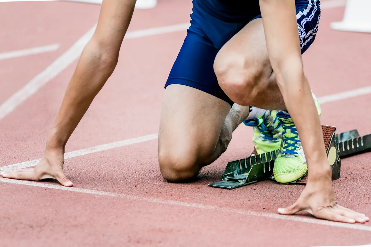 Läufer in der Startposition auf einer roten Tartanbahn, bereit für den Sprint.
