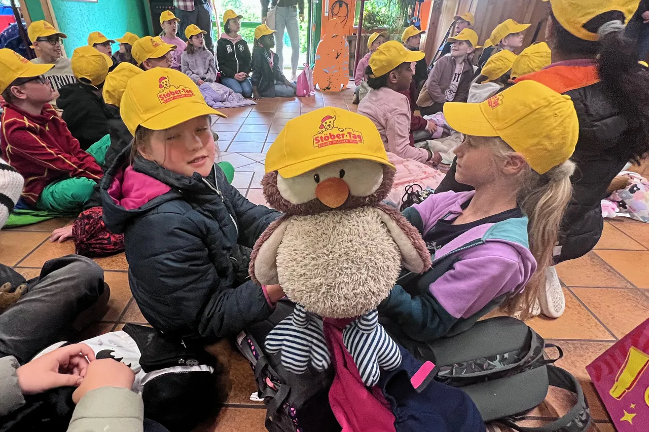 Kinder sitzen im Kreis auf dem Boden und warten auf ihre Aufgaben beim Stöbertag im Jugendzentrum. Viele tragen gelbe Kappen mit dem Aufdruck