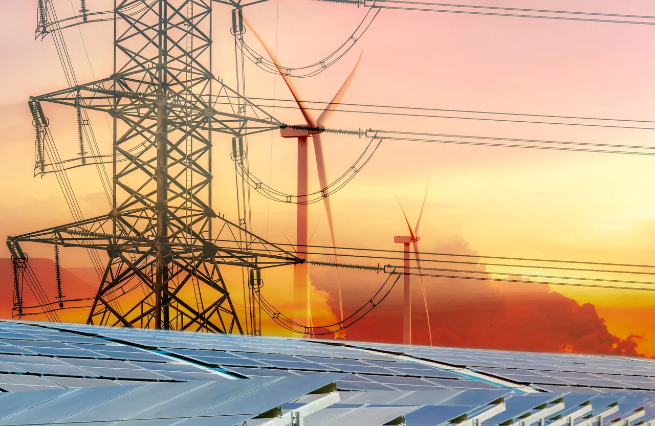 Solaranlage im Vordergrund, dahinter Windräder und ein Strommast vor einem orangefarbenen Himmel – Symbolbild für erneuerbare Energien.