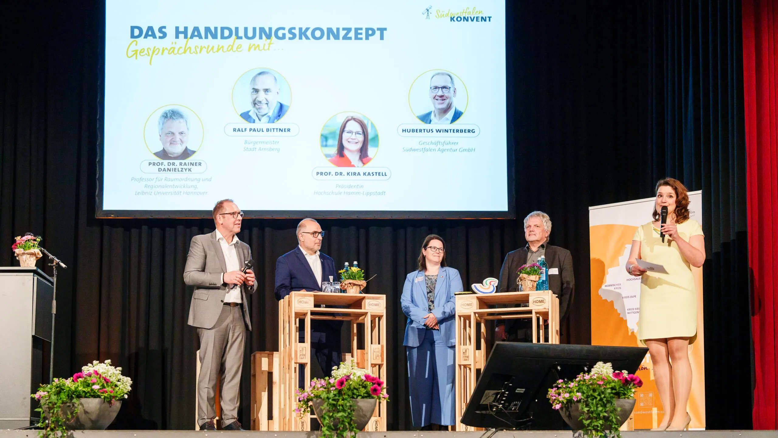 Auf einer Bühne diskutieren fünf Personen, darunter Hubertus Winterberg, Ralf Paul Bittner, Prof. Dr. Kira Kastell, Prof. Dr. Rainer Danielzyk und Marie Ting, vor einem Hintergrund mit dem Titel „Das Handlungskonzept“.