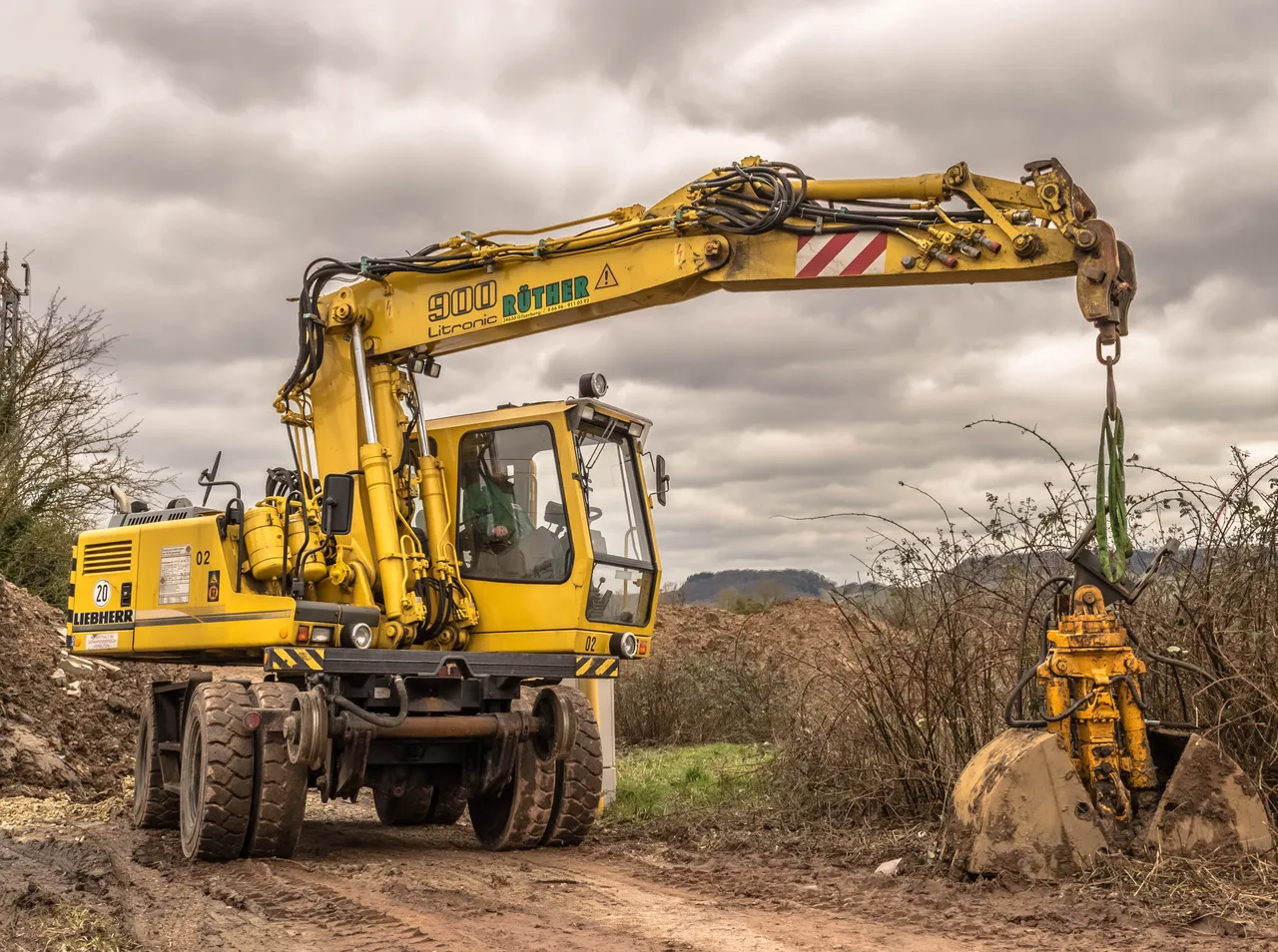 Ein gelber Liebherr-Bagger steht auf einem unbefestigten Weg unter einem bewölkten Himmel.