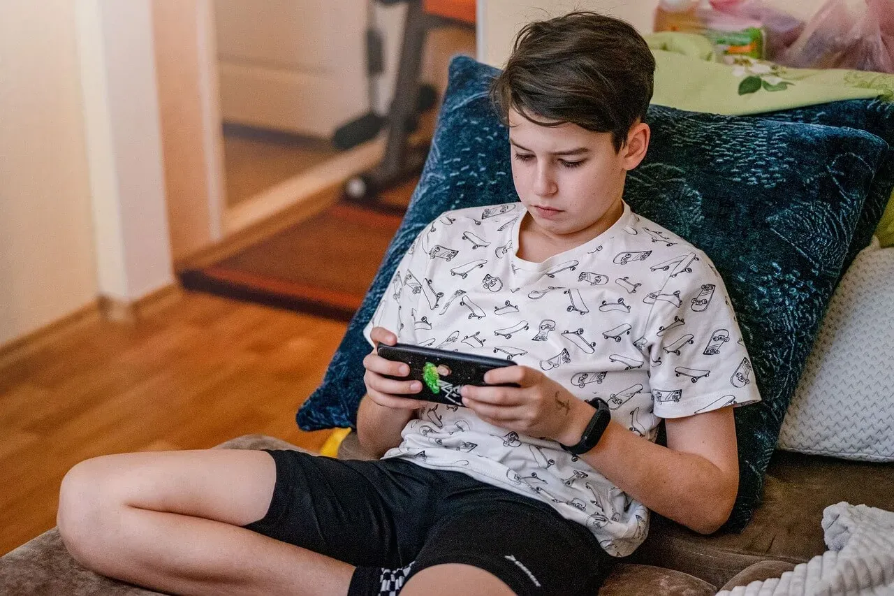 Ein Teenager sitzt auf einem Sofa und spielt auf einem Smartphone.
