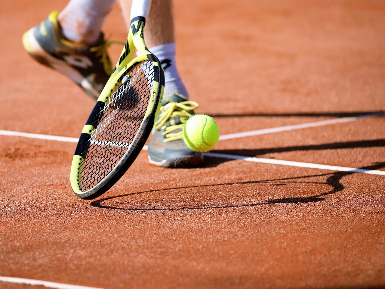Nahaufnahme eines gelben Tennisballs und eines Schlägers auf einem roten Sandplatz.