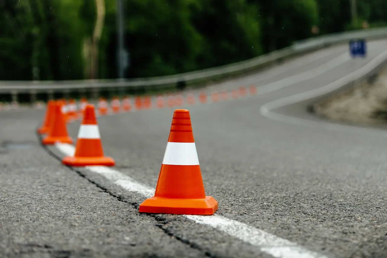 Orangefarbene Leitkegel mit weißen Streifen markieren den Verlauf einer kurvigen Asphaltstraße.