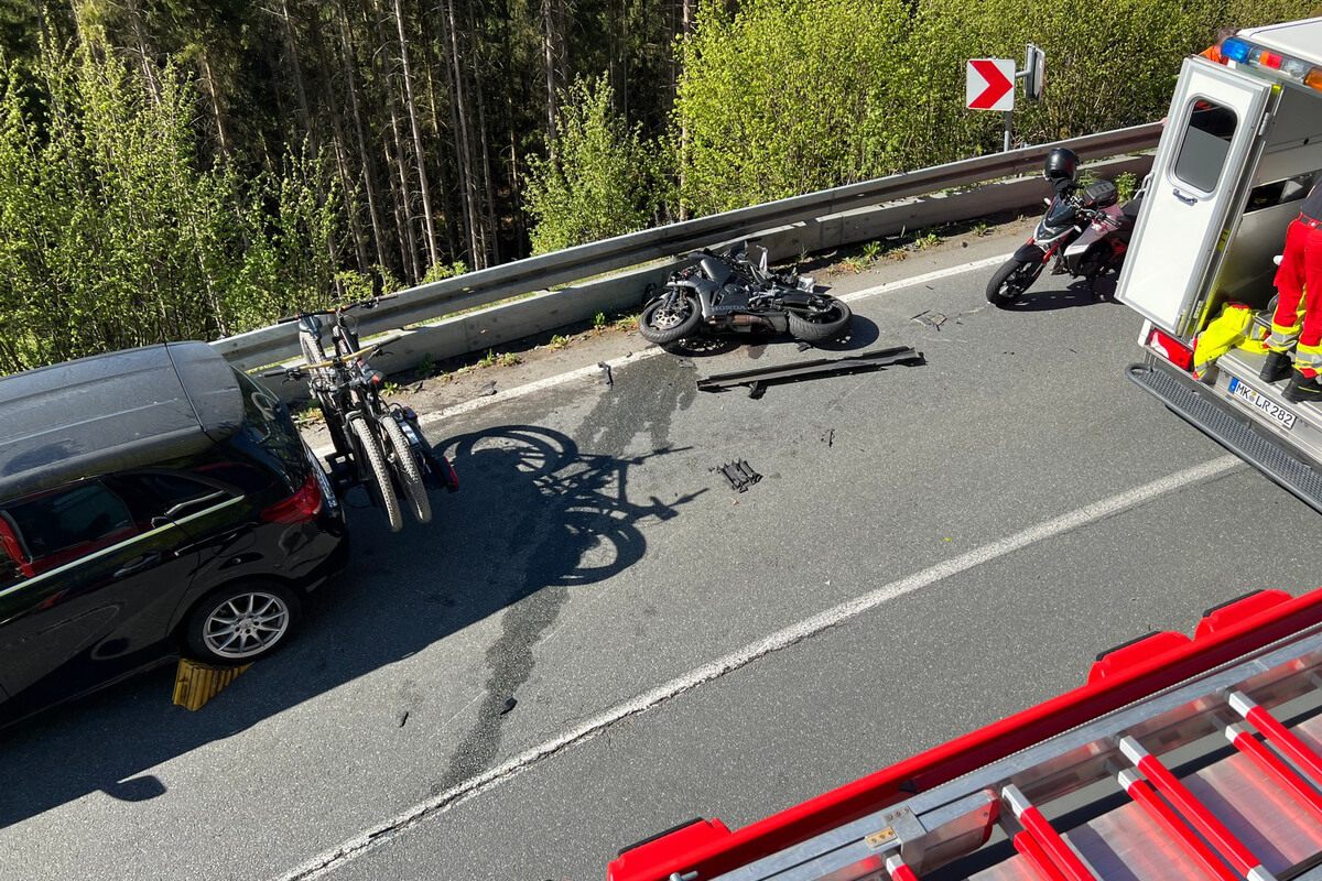 Motorrad liegt auf der Fahrbahn neben einem Auto und einem Abschleppwagen, vermutlich nach einem Unfall. Im Hintergrund Bäume und Leitplanken.