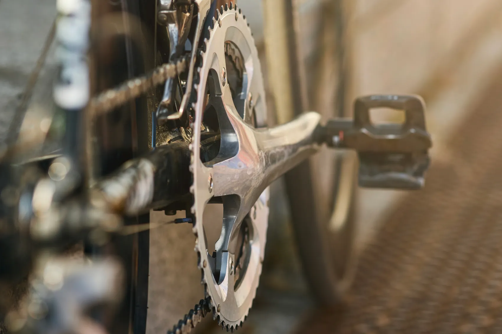 Nahaufnahme der Tretkurbel und Kettenblätter eines Fahrrads. Die silbernen Metallteile stehen im Fokus, während der Hintergrund unscharf ist.