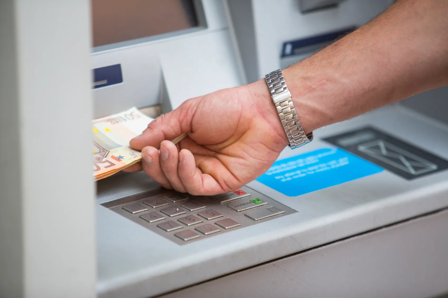 Eine Hand entnimmt Euro-Banknoten aus einem Geldautomaten.